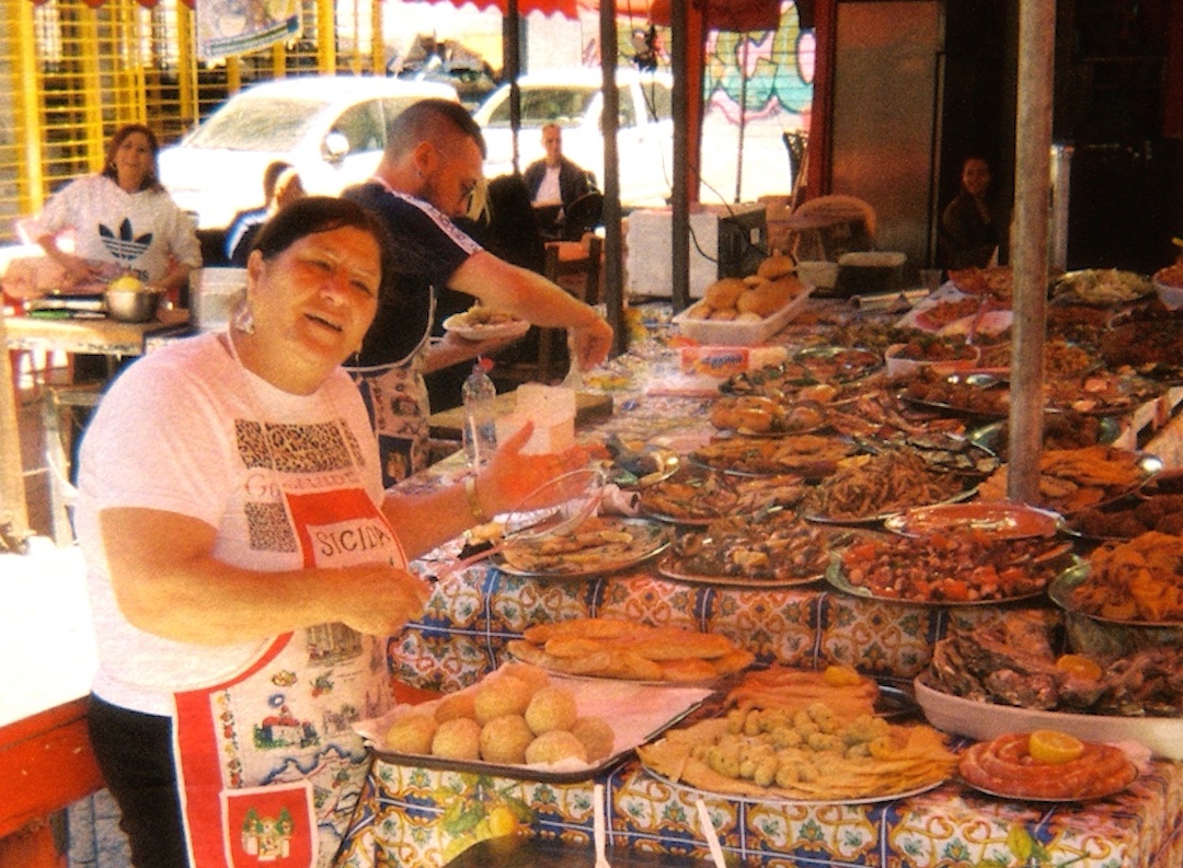 Une vendeuse de street food sicilienne devant son étal de poisson frit et d'arancini, Palerme