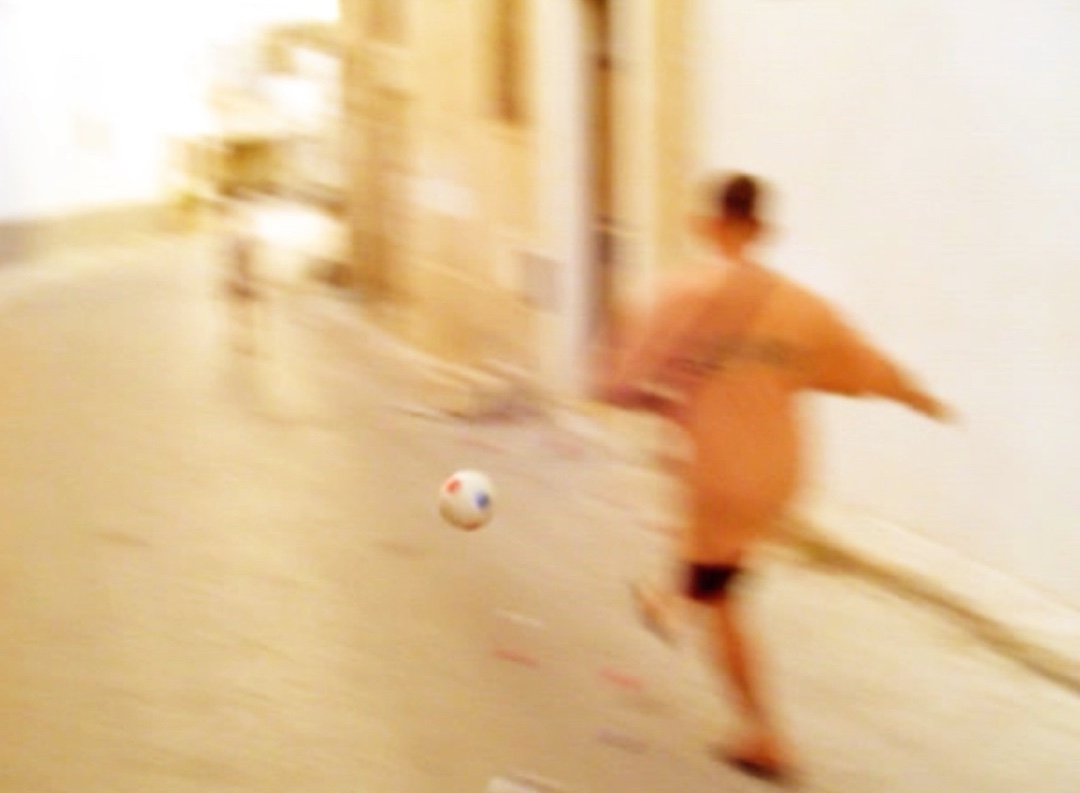 Un enfant court après un ballon dans une ruelle écrasée de soleil, film de rue en Tunisie