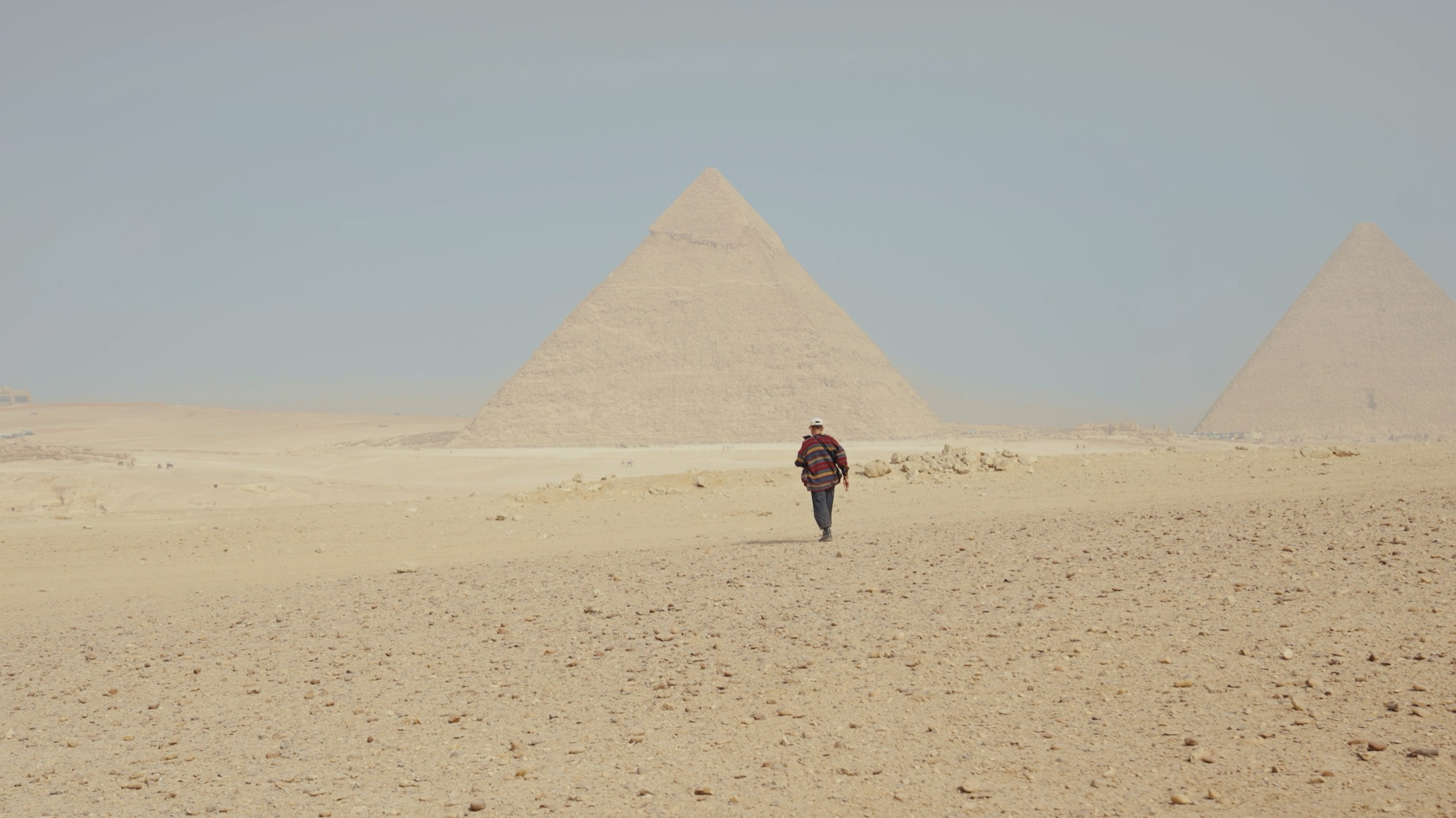 Un homme marche seul dans le désert vers les pyramides de Gizeh, dans la brume de chaleur.