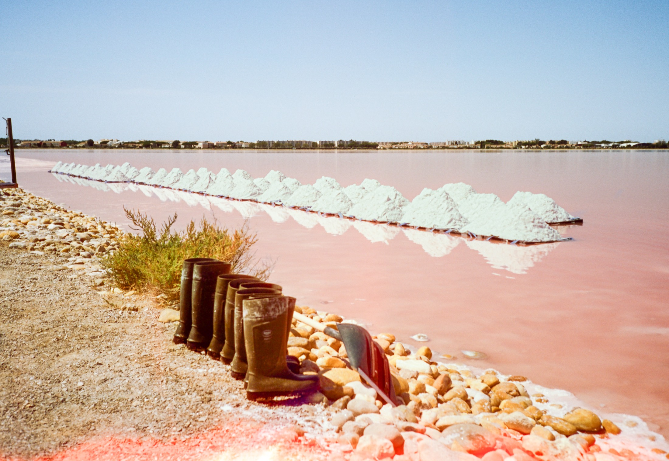 Bottes alignées au bord d'une table salante rose, camelles de sel blanc au loin, en Camargue.