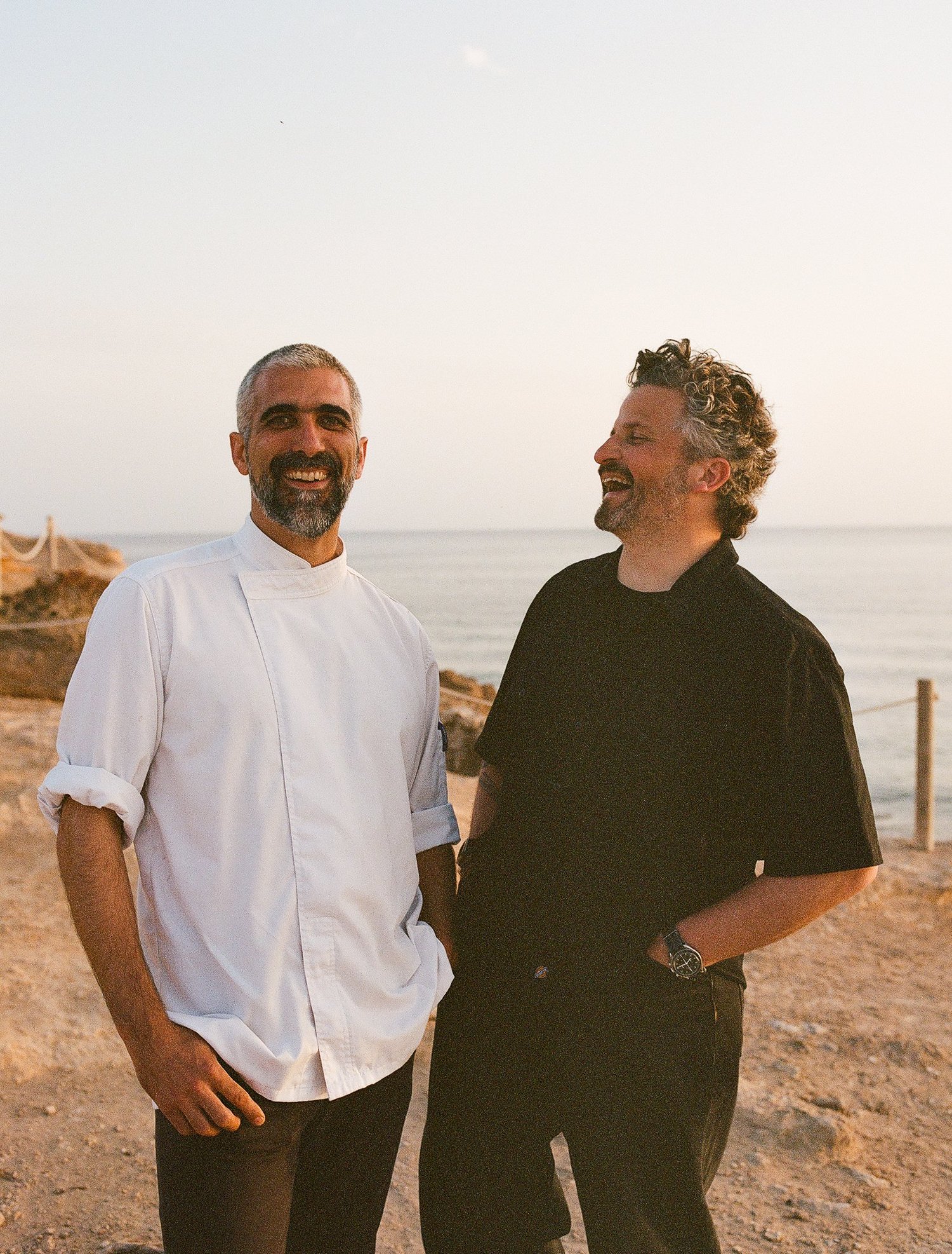 Le chef en veste blanche rit avec un homme au bord de la mer, Ibiza