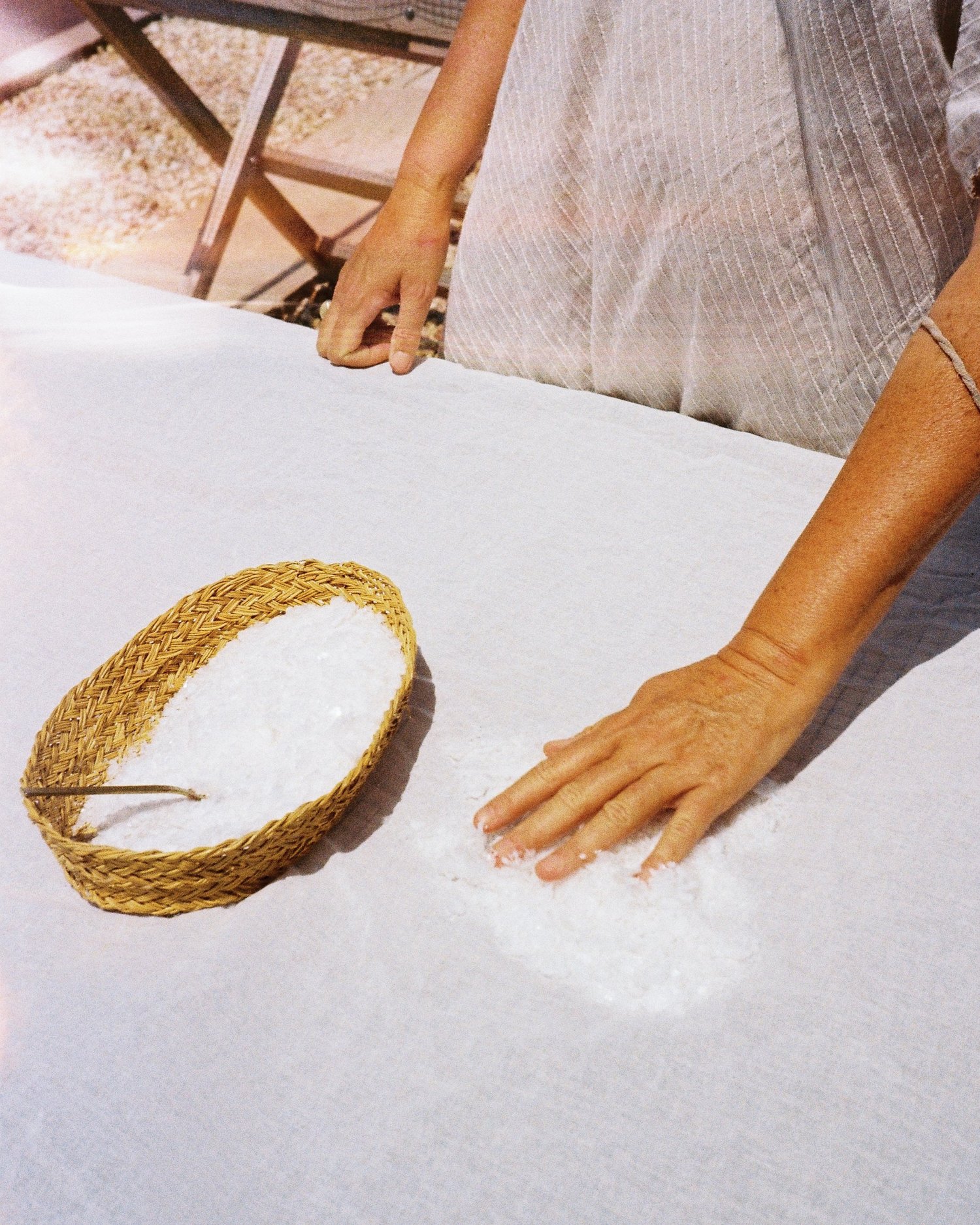 Des mains étalent le sel récolté sur une toile blanche, à côté d'un panier tressé, Minorque