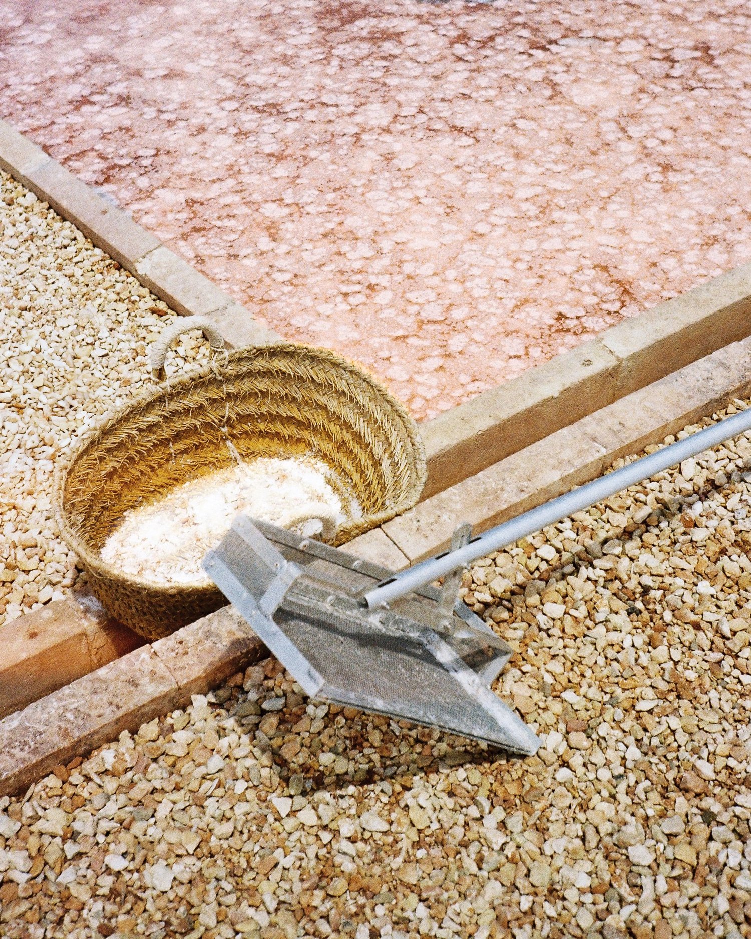 Panier tressé et racloir posés au bord d'un bassin de sel rose, salines de Minorque
