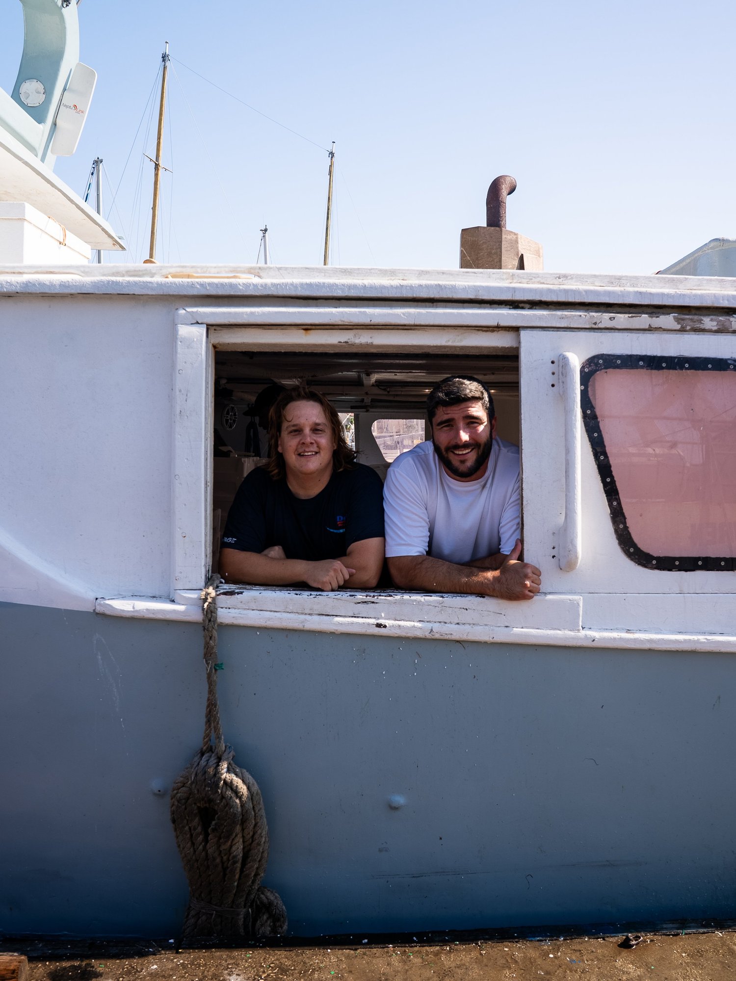 Deux marins de Côté Fish accoudés à la fenêtre de la timonerie, au Grau-du-Roi