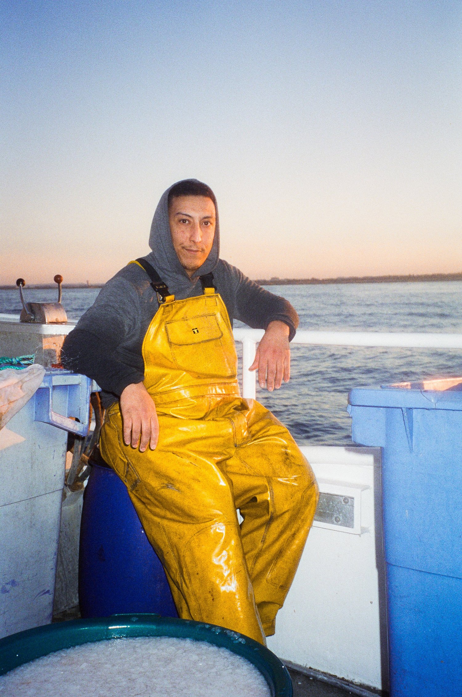 Un marin en ciré jaune assis sur le pont au crépuscule, bateau de Côté Fish