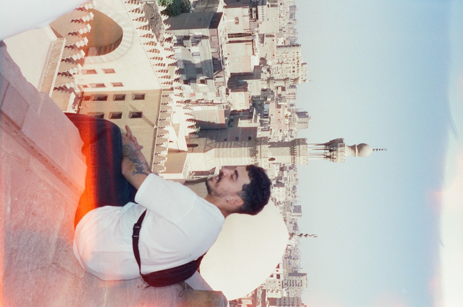Un homme assis sur un toit devant les minarets et les immeubles du Caire