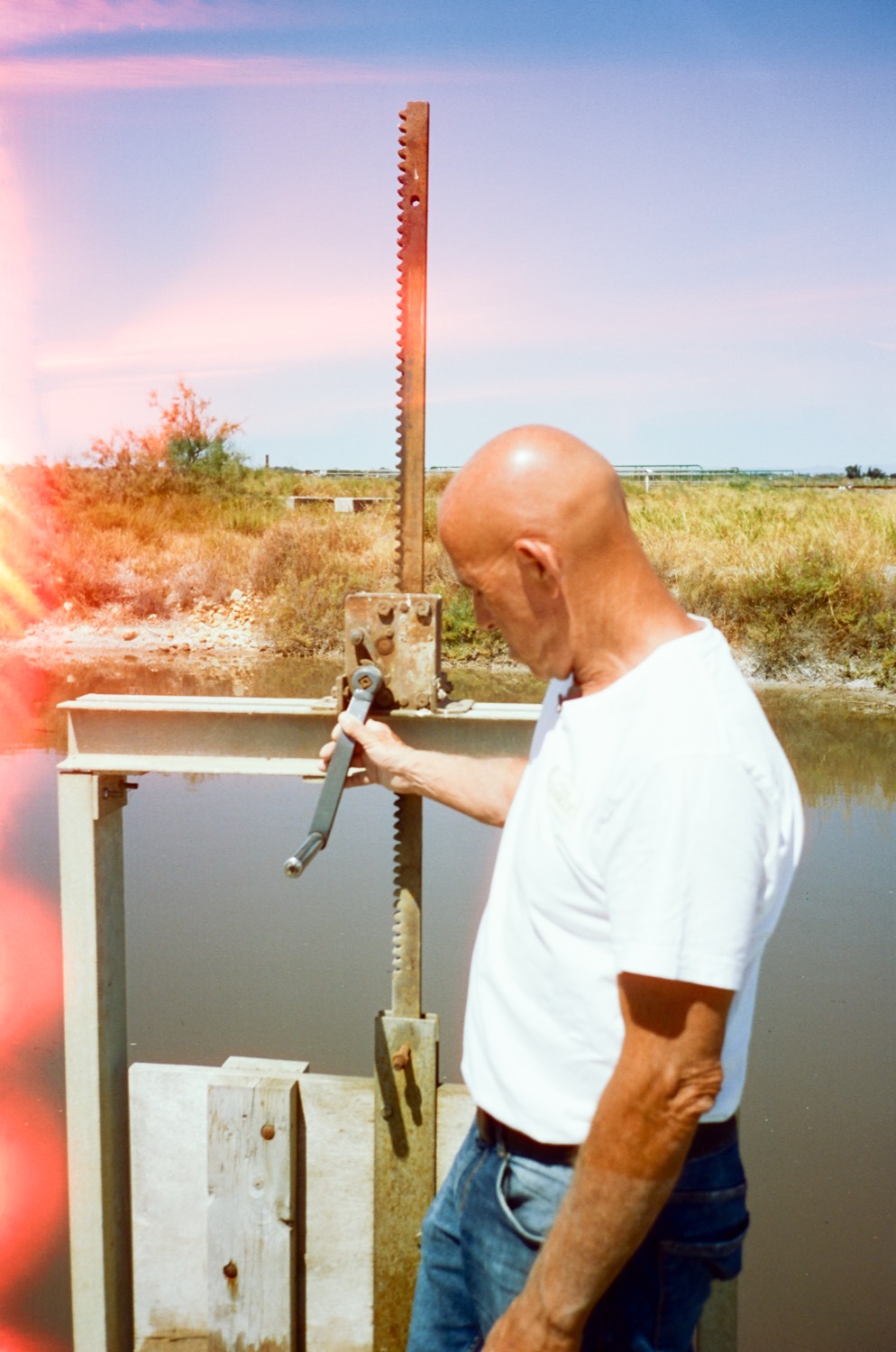 Un saunier manoeuvre une vanne à la manivelle au bord d'un canal, salins de Camargue