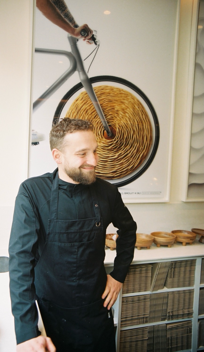 Un pâtissier sourit devant l'affiche d'une tarte roulée, boutique de Cédric Grolet à Paris