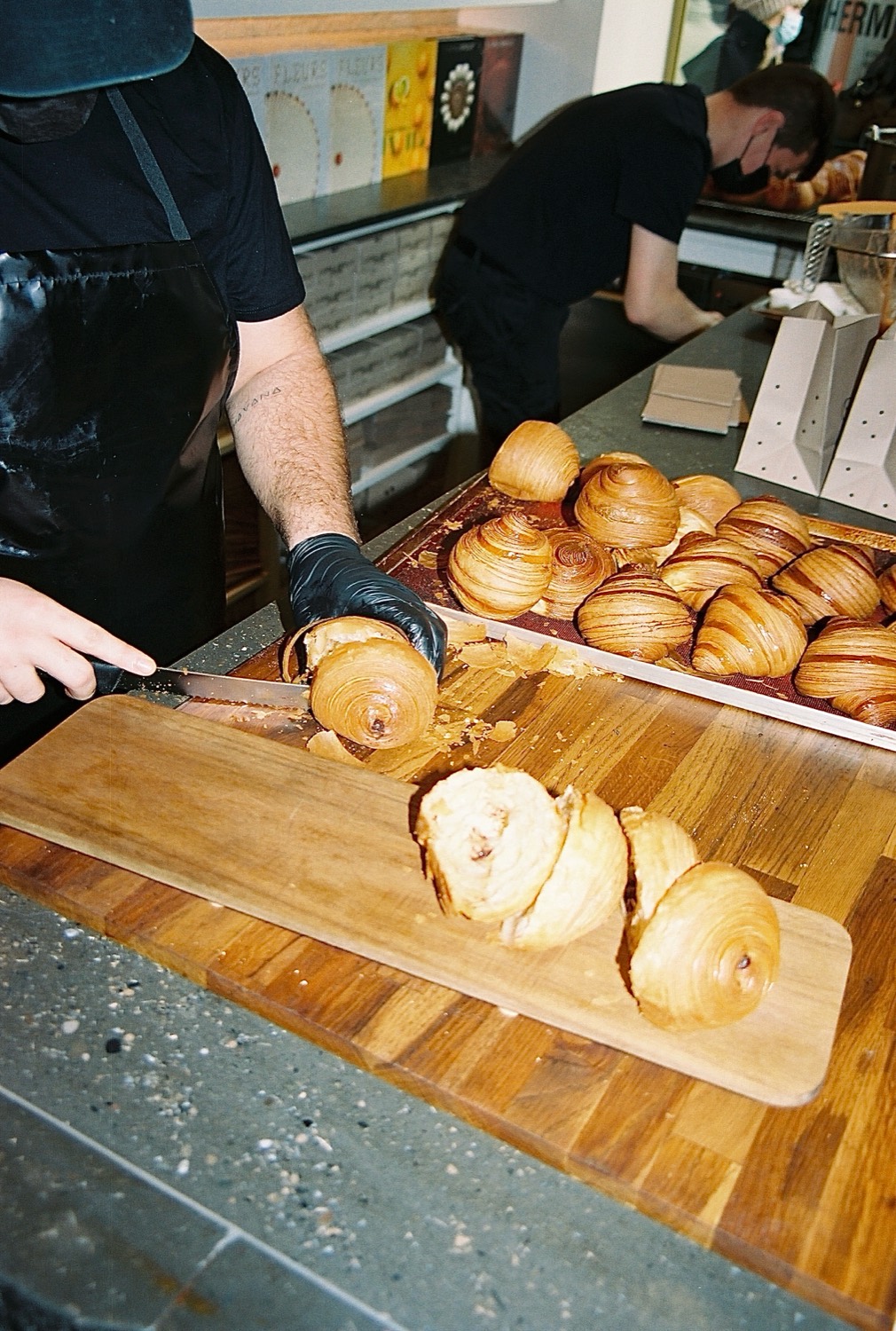 Un pâtissier tranche des croissants feuilletés sur une planche de bois, maison Cédric Grolet, Paris