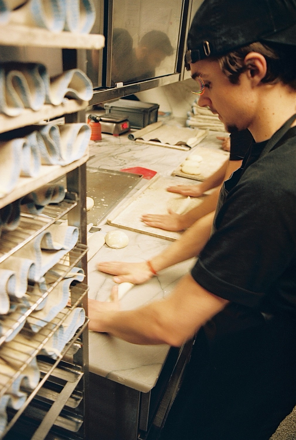 Un boulanger façonne la pâte au marbre devant les échelles du fournil, maison Cédric Grolet