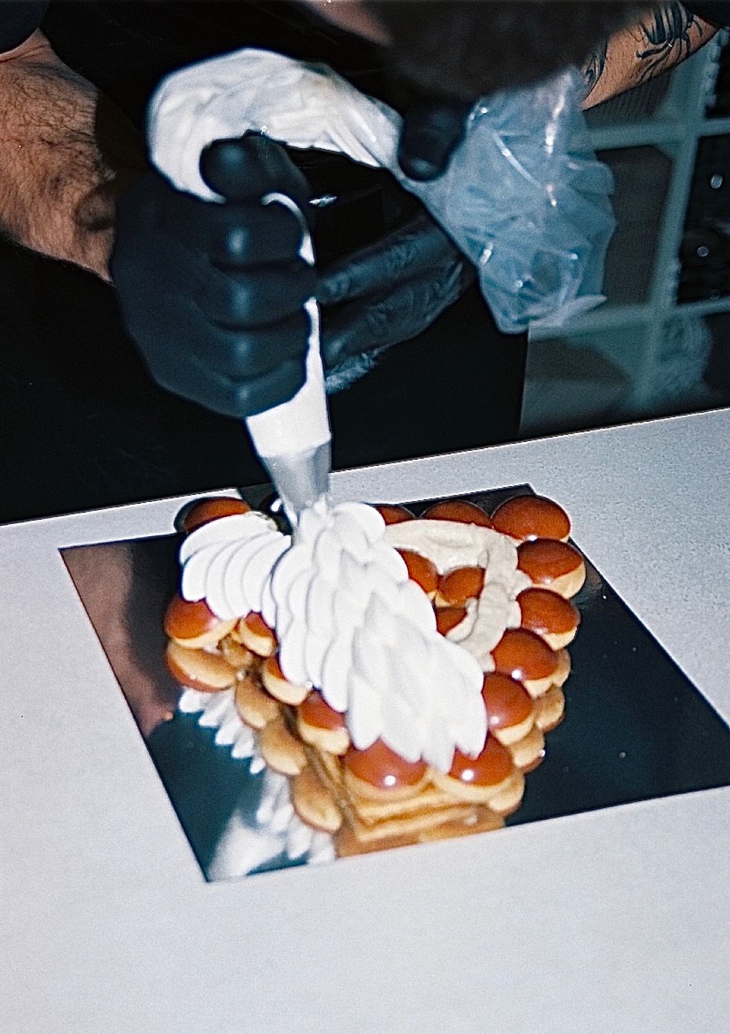 Une main gantée poche la crème sur un gâteau aux choux, maison Cédric Grolet, Paris
