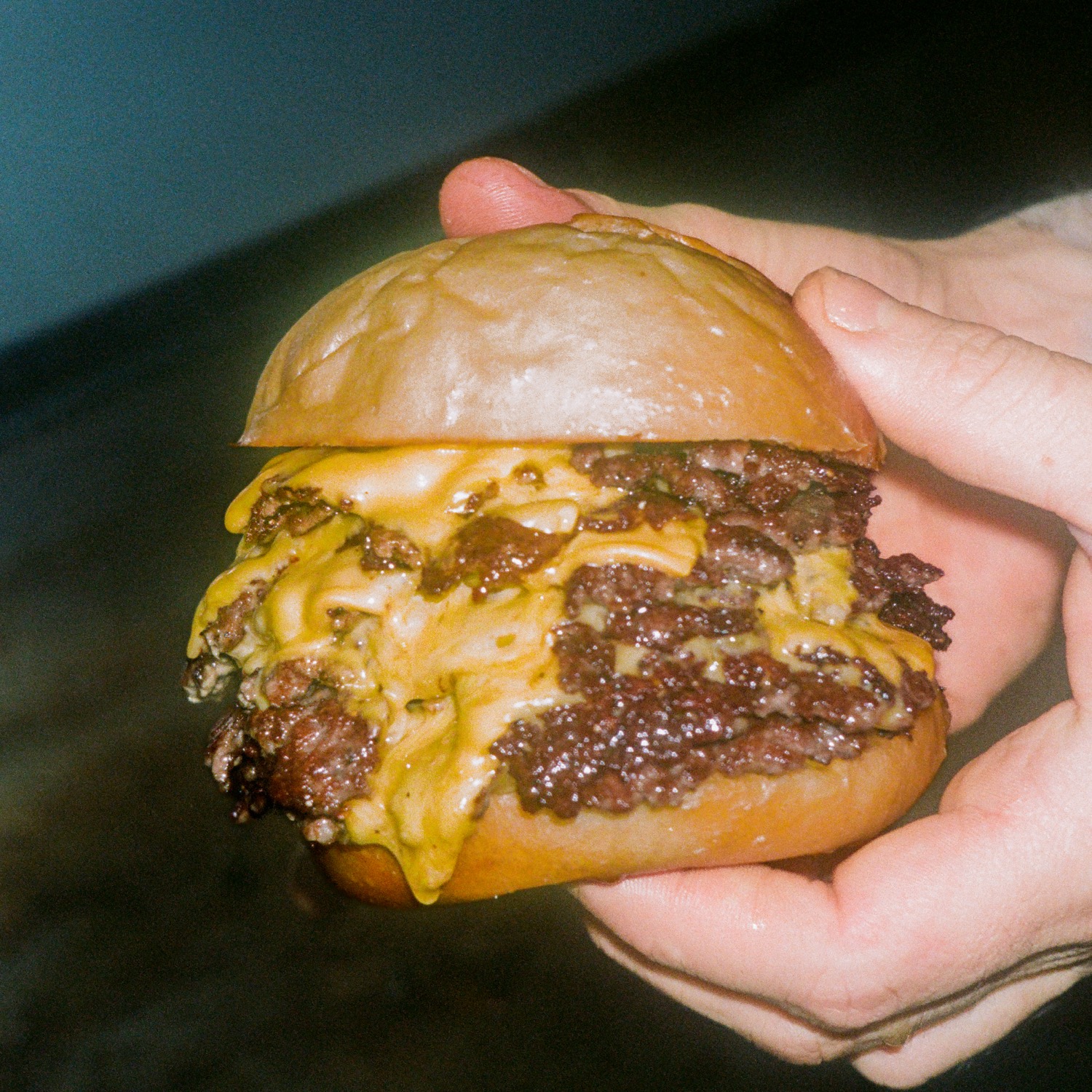 Deux mains présentent un double cheeseburger au cheddar débordant, Howard Original