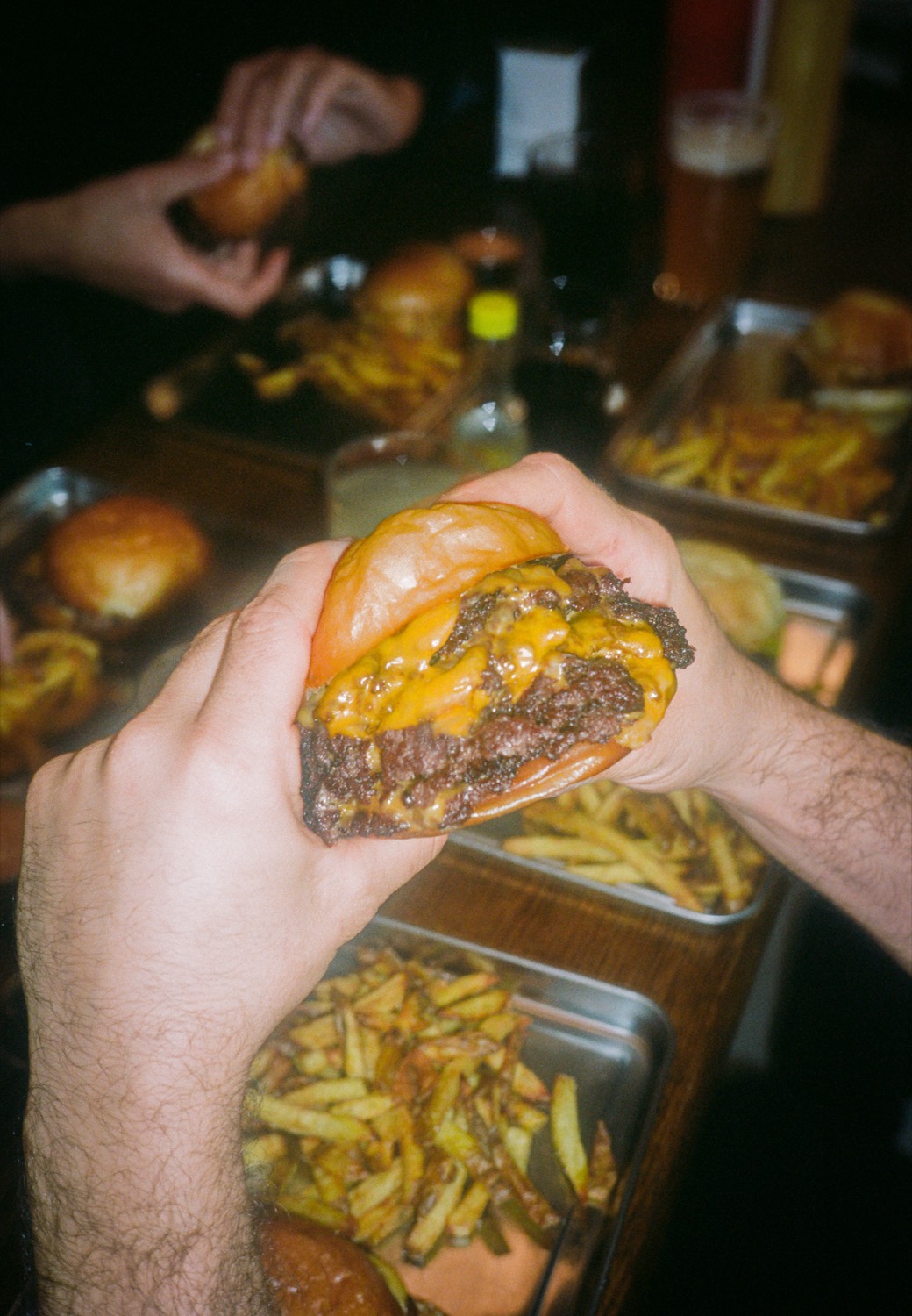 Des mains soulèvent un double cheeseburger au-dessus des plateaux de frites, Howard Original