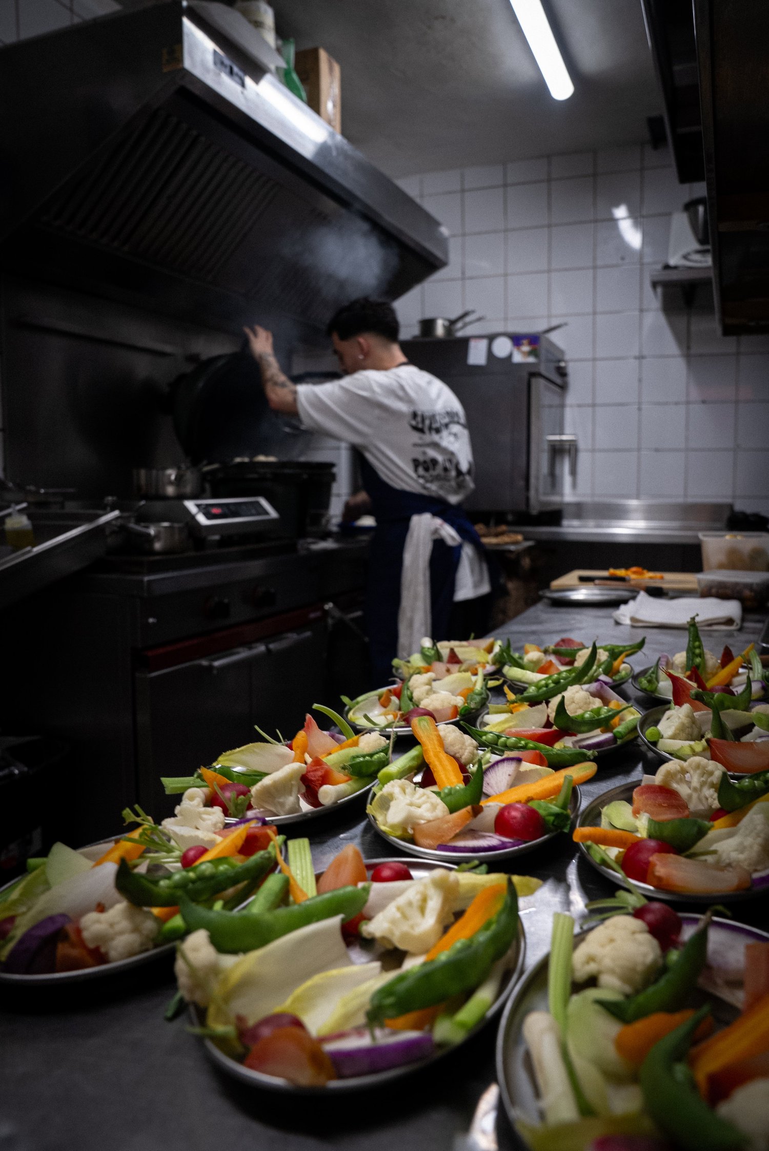 Plats de crudités alignés au premier plan, un cuisinier aux fourneaux derrière, Livingston, Marseille