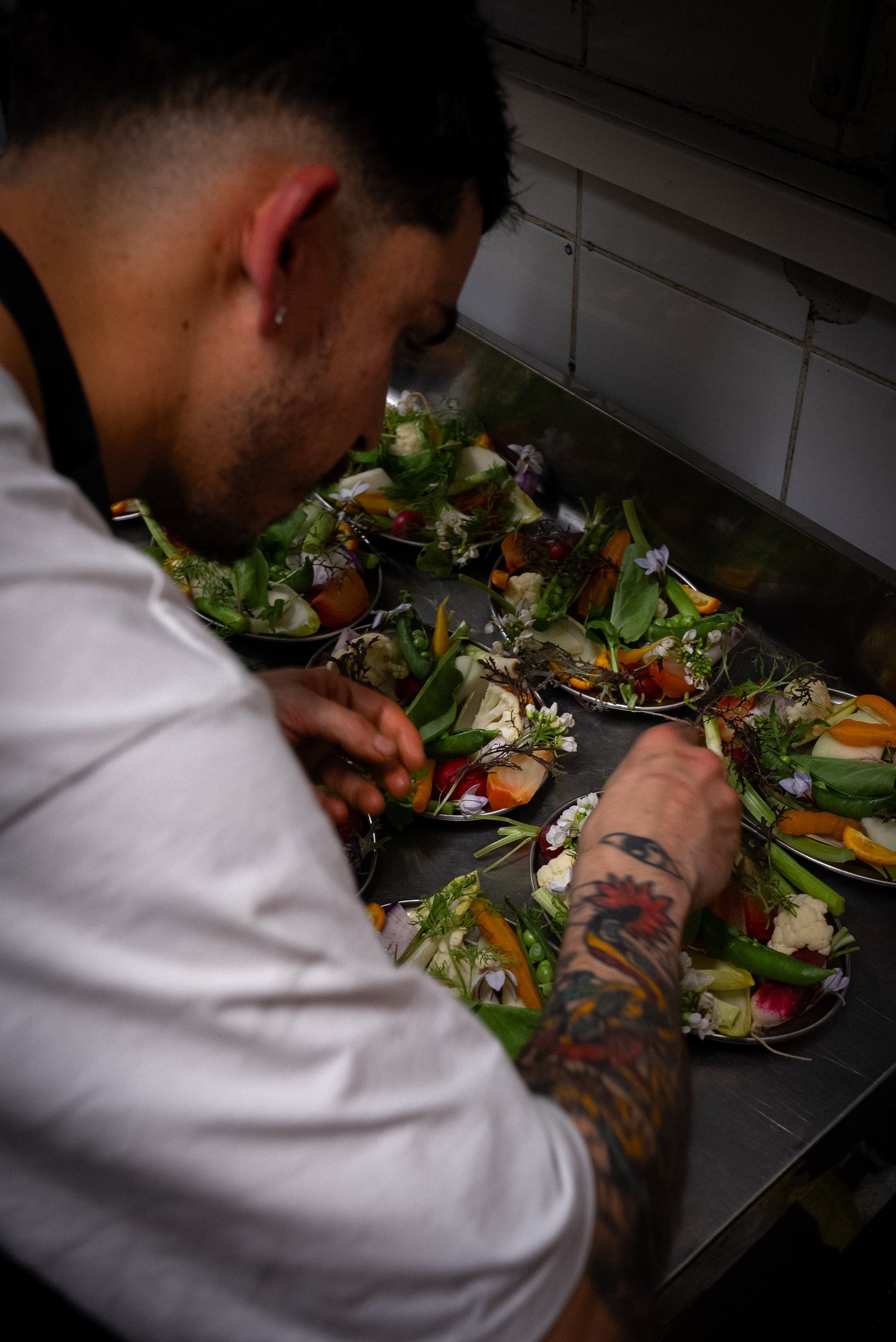 Un cuisinier dresse des assiettes de crudités et de fleurs, avant-bras tatoué, Livingston, Marseille