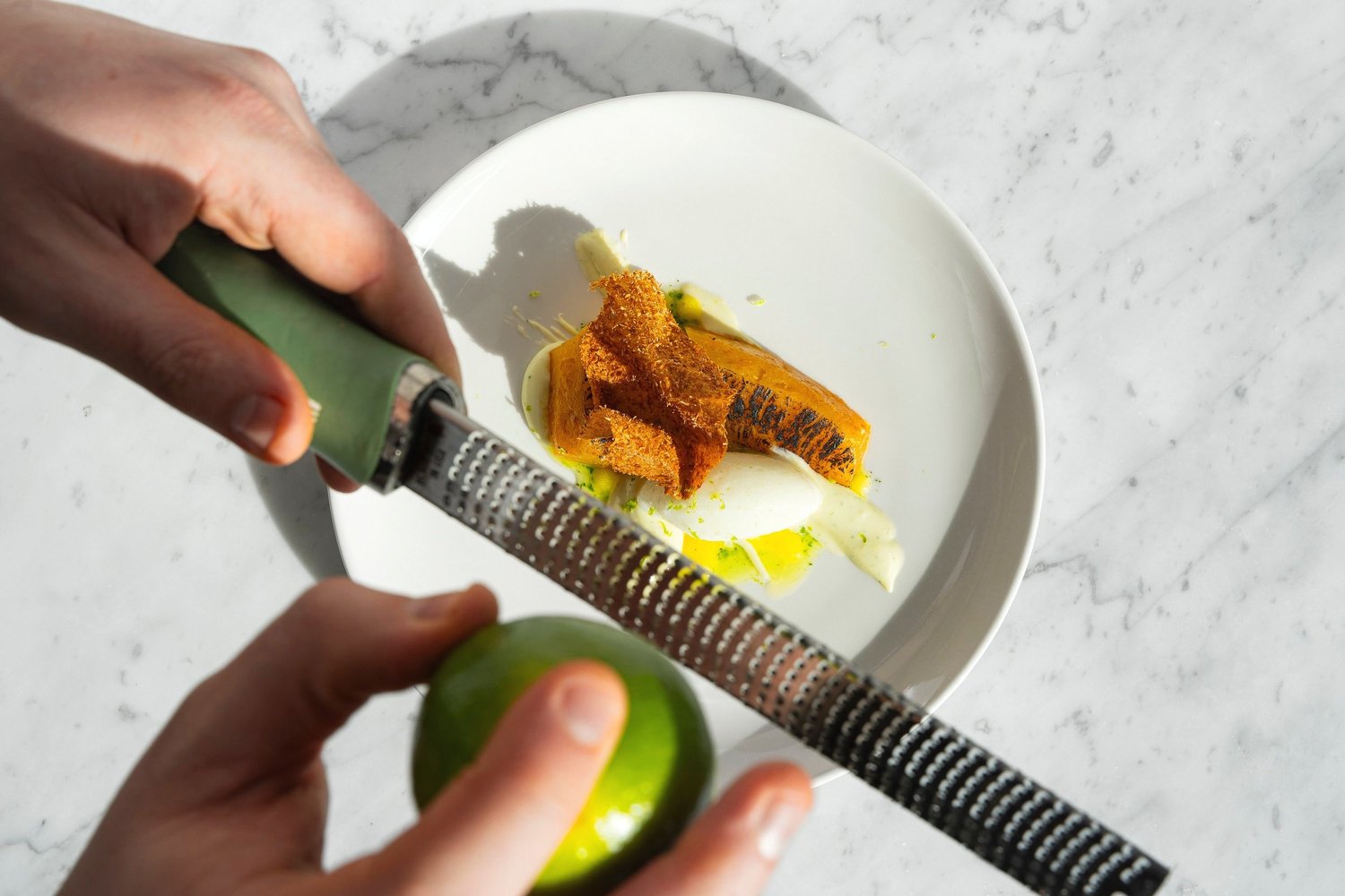 Une main râpe le zeste d'un citron vert sur une assiette de poisson grillé, hôtel Nhow, Marseille