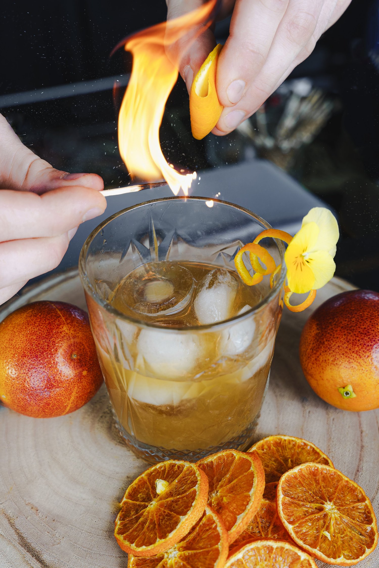 Des mains flambent un zeste d'orange au-dessus d'un cocktail sur glace, bar du Nhow, Marseille