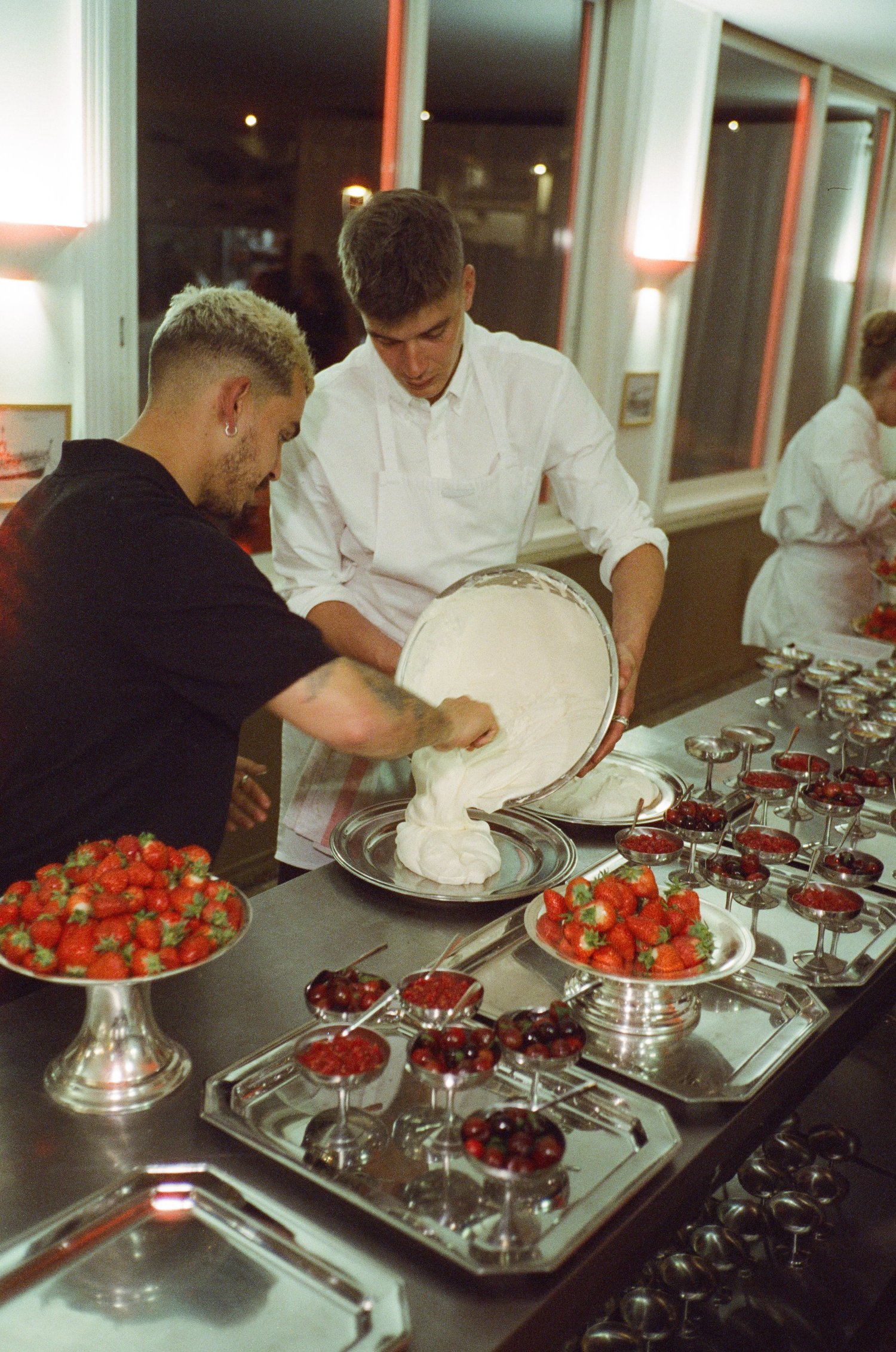 Deux cuisiniers versent la crème fouettée près des coupes de fraises, dîner Chanel