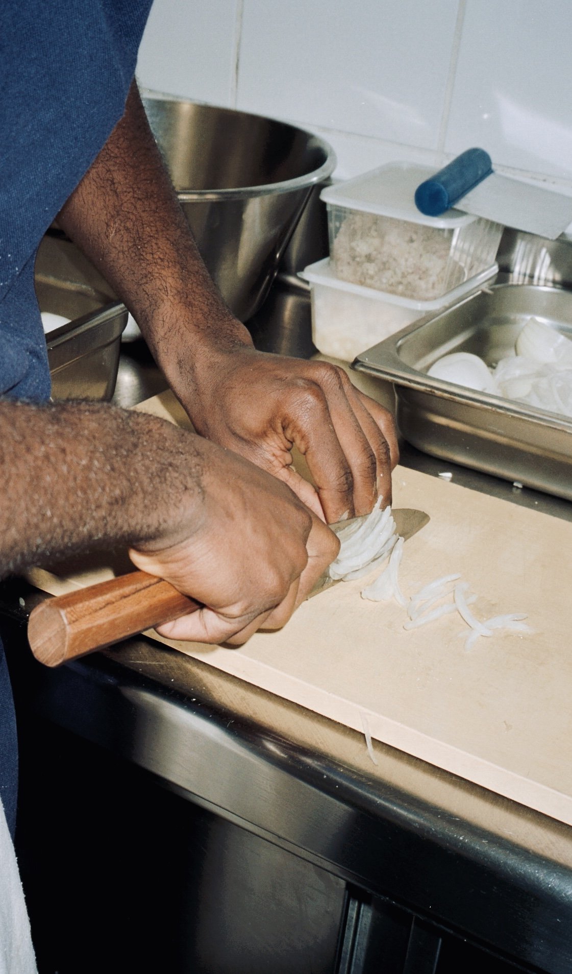 Des mains émincent un oignon au couteau sur une planche, cuisine du restaurant