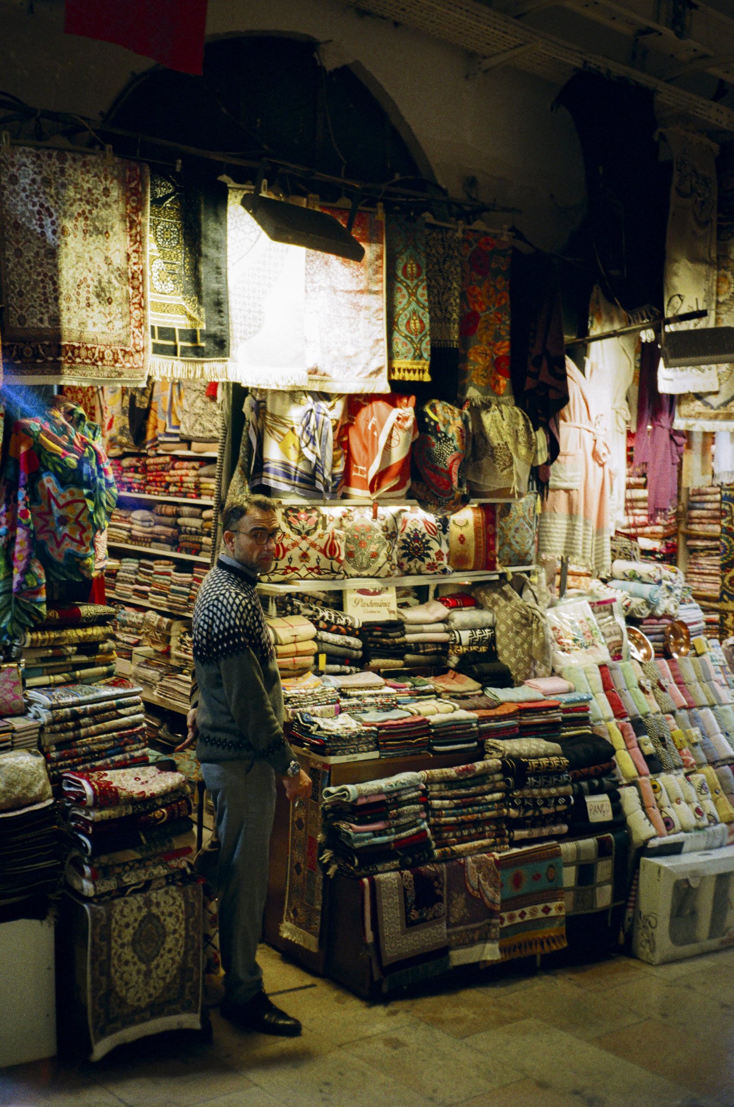 Un marchand debout au milieu de ses tapis et de ses tissus empilés, bazar d'Istanbul