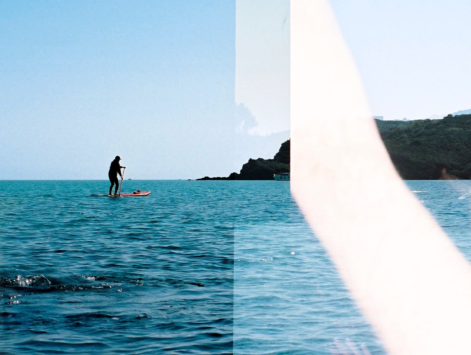 Un paddle glisse sur une mer turquoise, la pellicule voilée sur la moitié de l'image