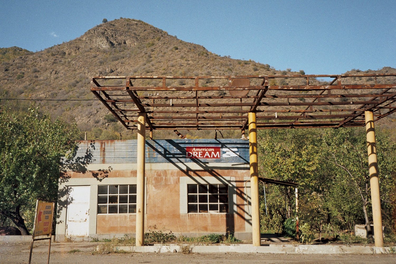 Ancienne station-service abandonnée au pied d'une colline, panneau American Dream, Arménie