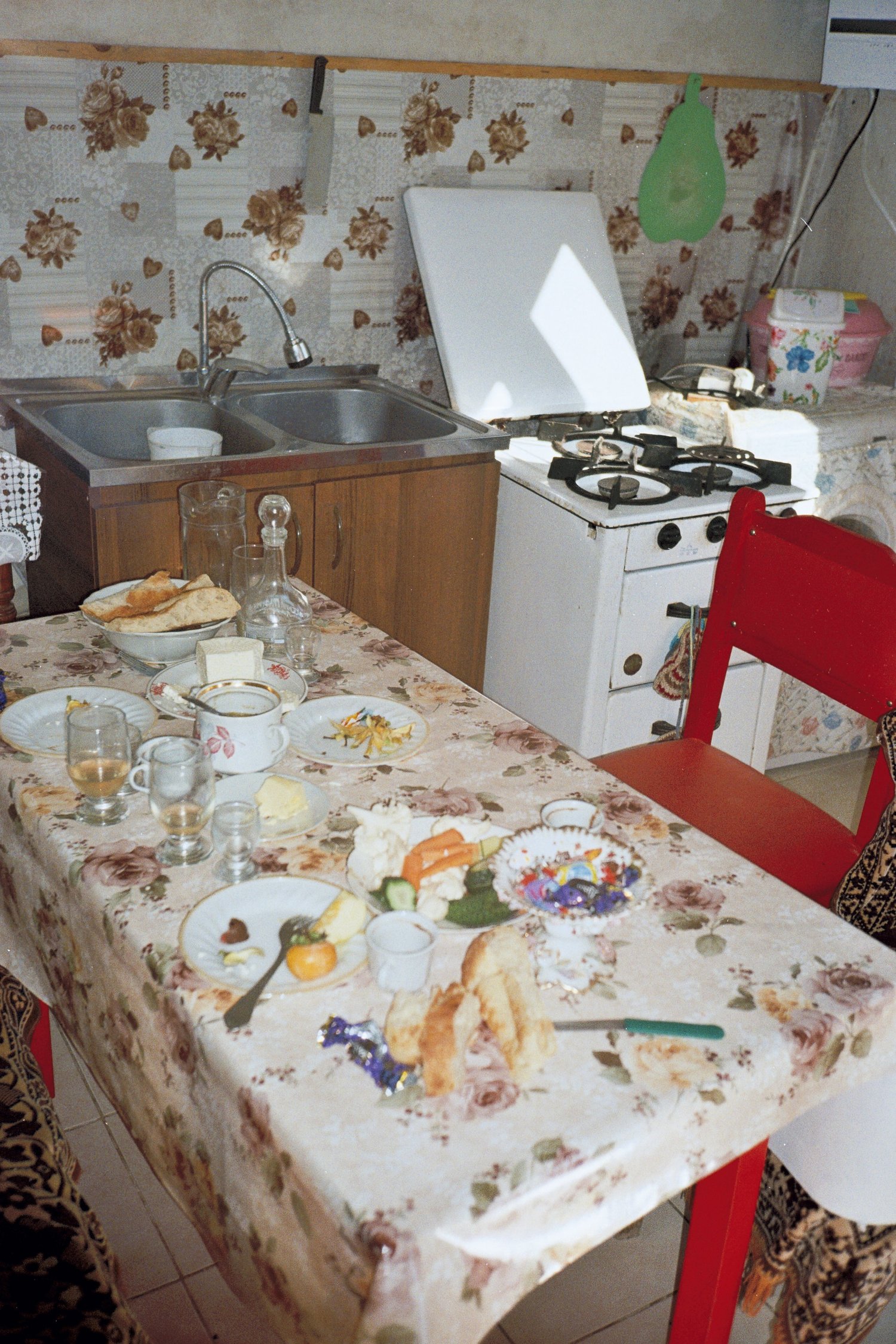 Table de cuisine à la nappe fleurie après le repas, cuisinière blanche et chaise rouge