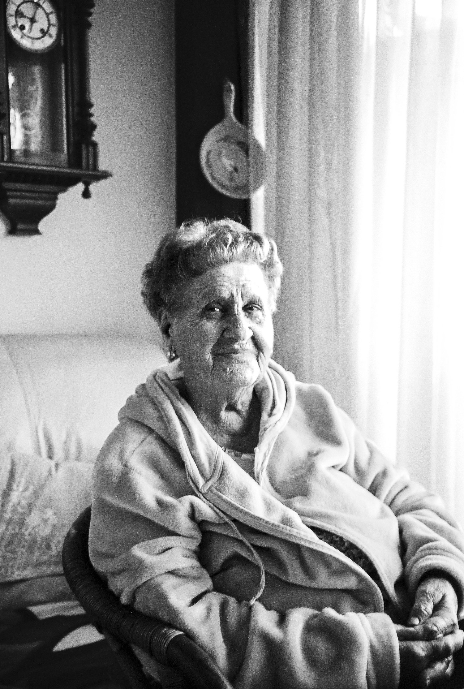 Portrait en noir et blanc d'une femme âgée assise près de la fenêtre, horloge au mur
