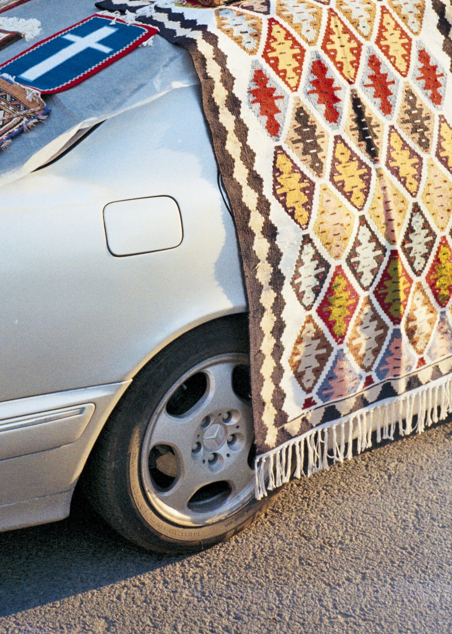 Tapis tissé étendu sur le capot d'une voiture grise, au bord de la route