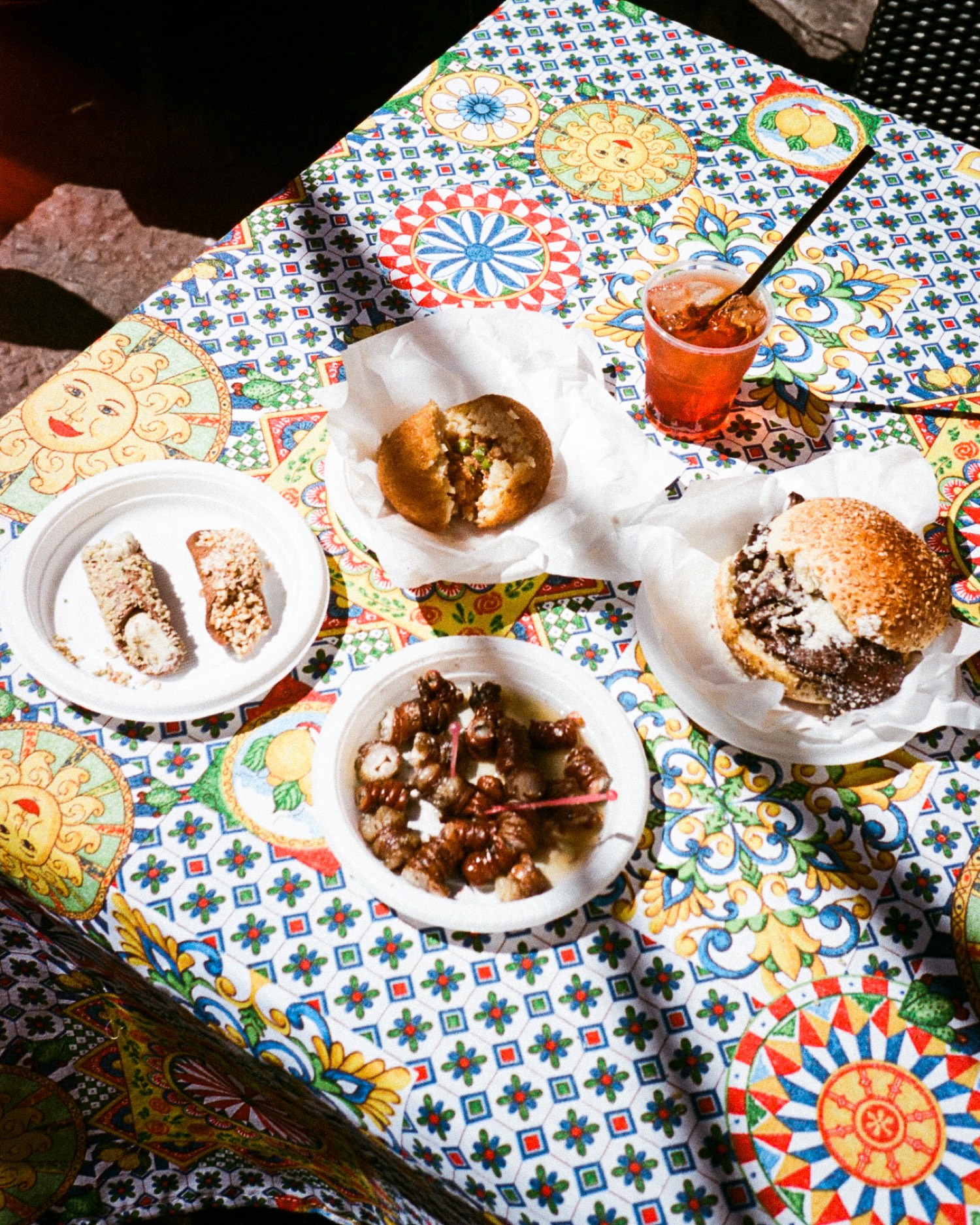 Table de street food sicilienne sur une nappe à motifs, arancino, cannoli, panino et escargots