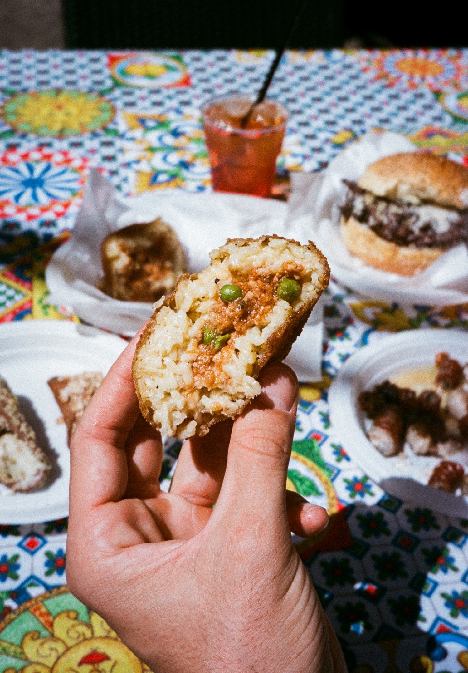 Un arancino ouvert en deux dans la main, riz, ragù et petits pois, street food de Palerme