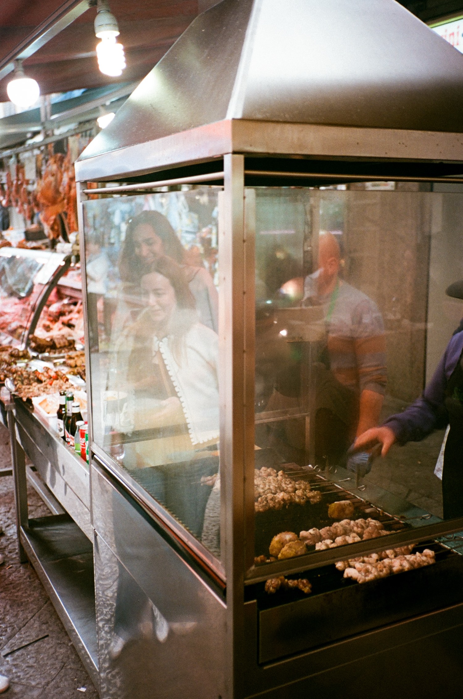 Des passants regardent griller la viande derrière la vitre d'un rôtissoir de marché, Palerme