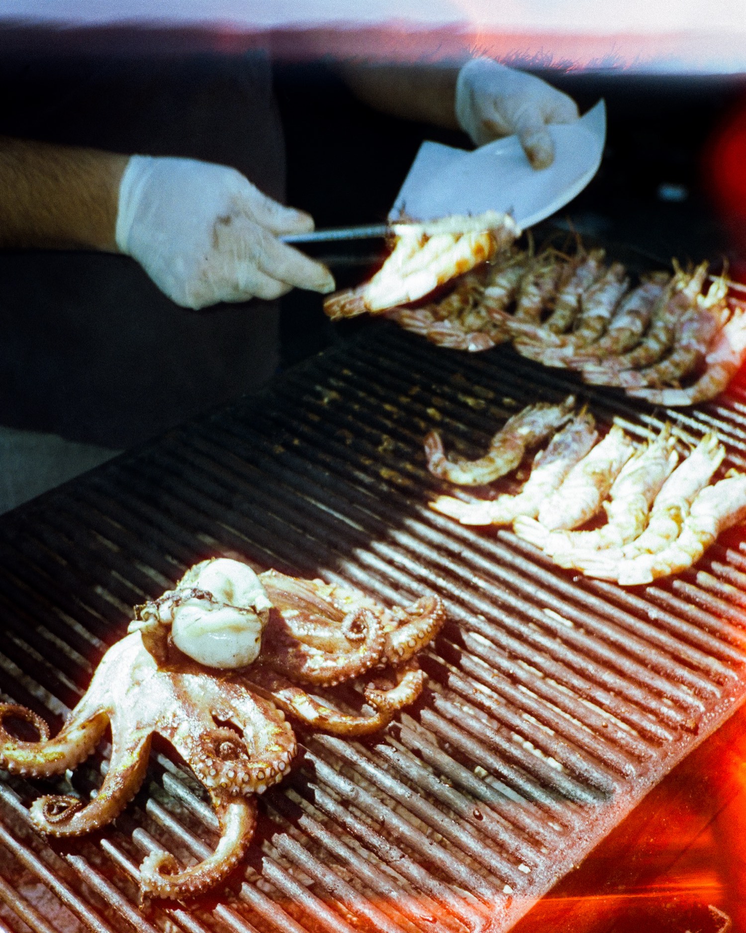 Gambas et poulpe sur le grill d'un stand de marché, mains gantées et pinces, Sicile