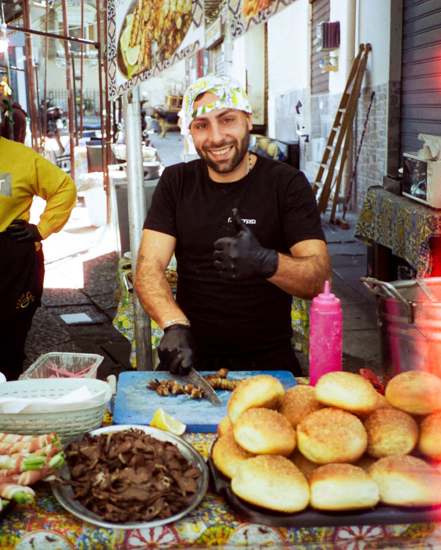 Un jeune cuisinier sourit derrière ses pains à sésame et sa viande, stand de rue à Palerme