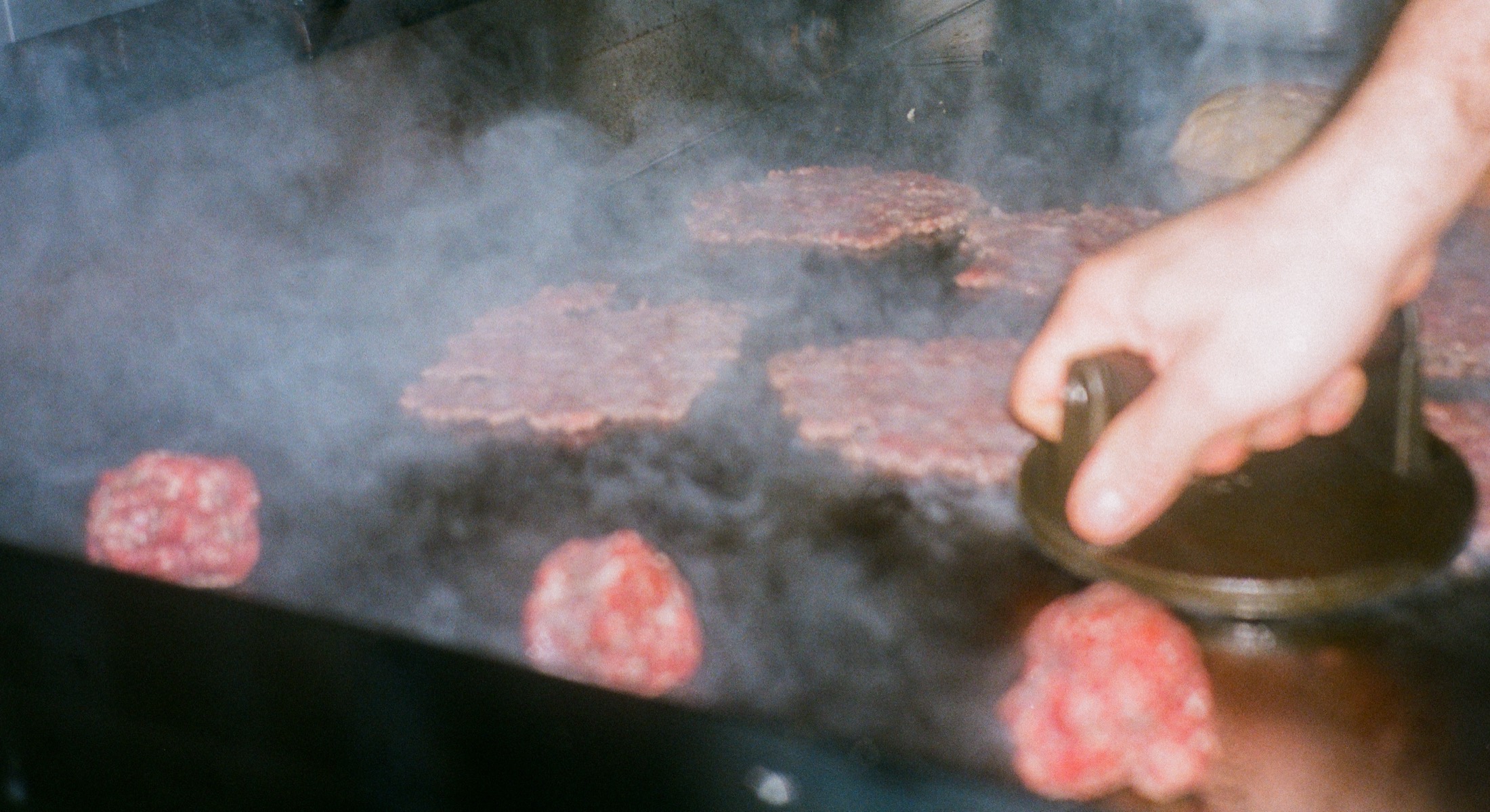 Des steaks hachés s'écrasent sur la plancha fumante sous la presse d'un cuisinier.