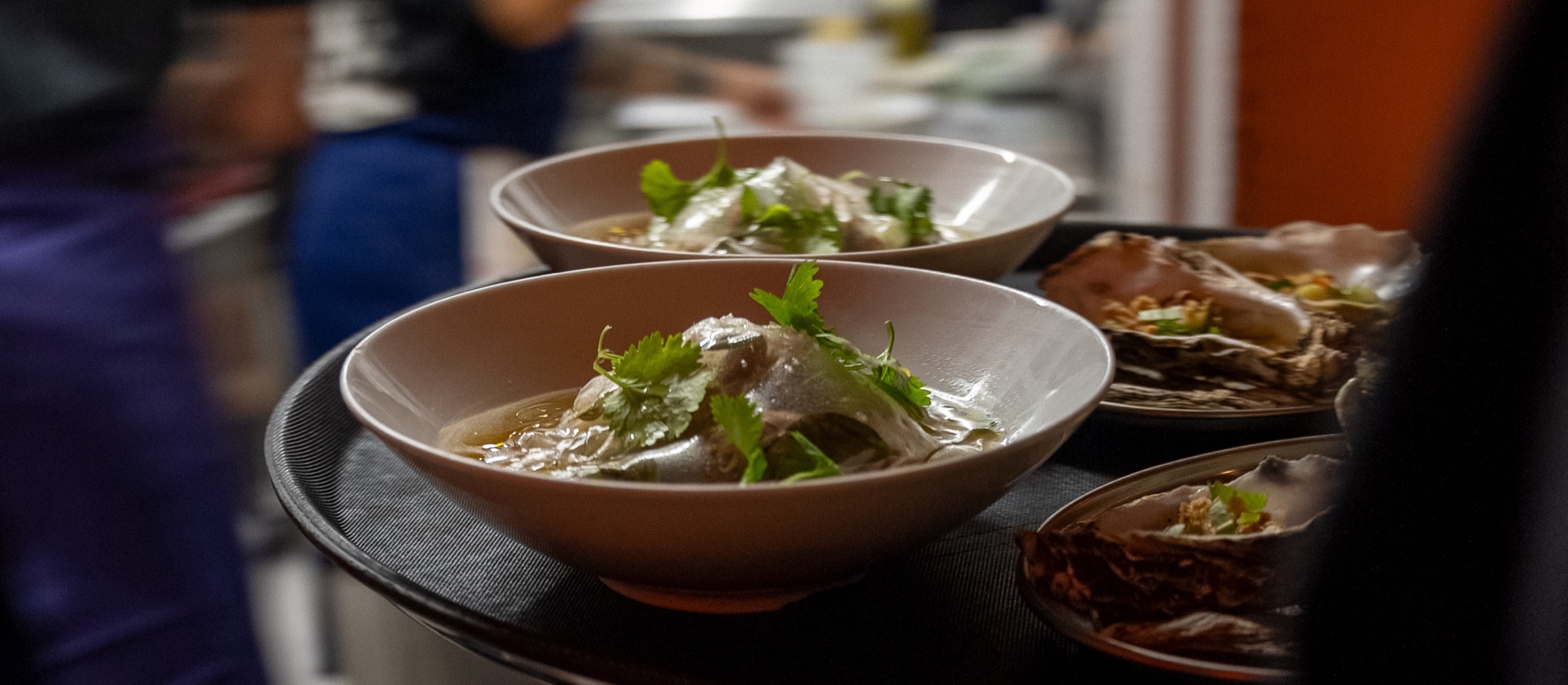 Deux bols de bouillon aux herbes fraîches attendent sur le plateau, au passe de la cuisine.